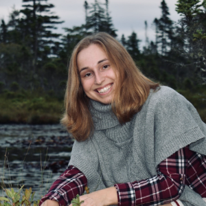 A woman posing for a photo in front of some trees and a lake