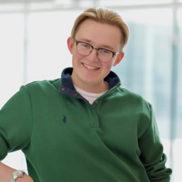 Jack Thistle posing for a photo wearing glasses and a green sweater