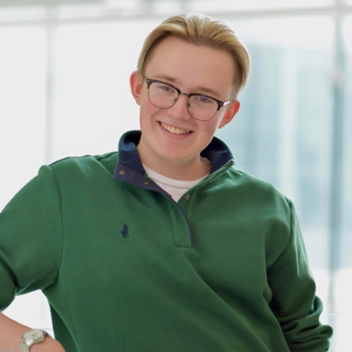 Jack Thistle posing for a photo wearing glasses and a green sweater