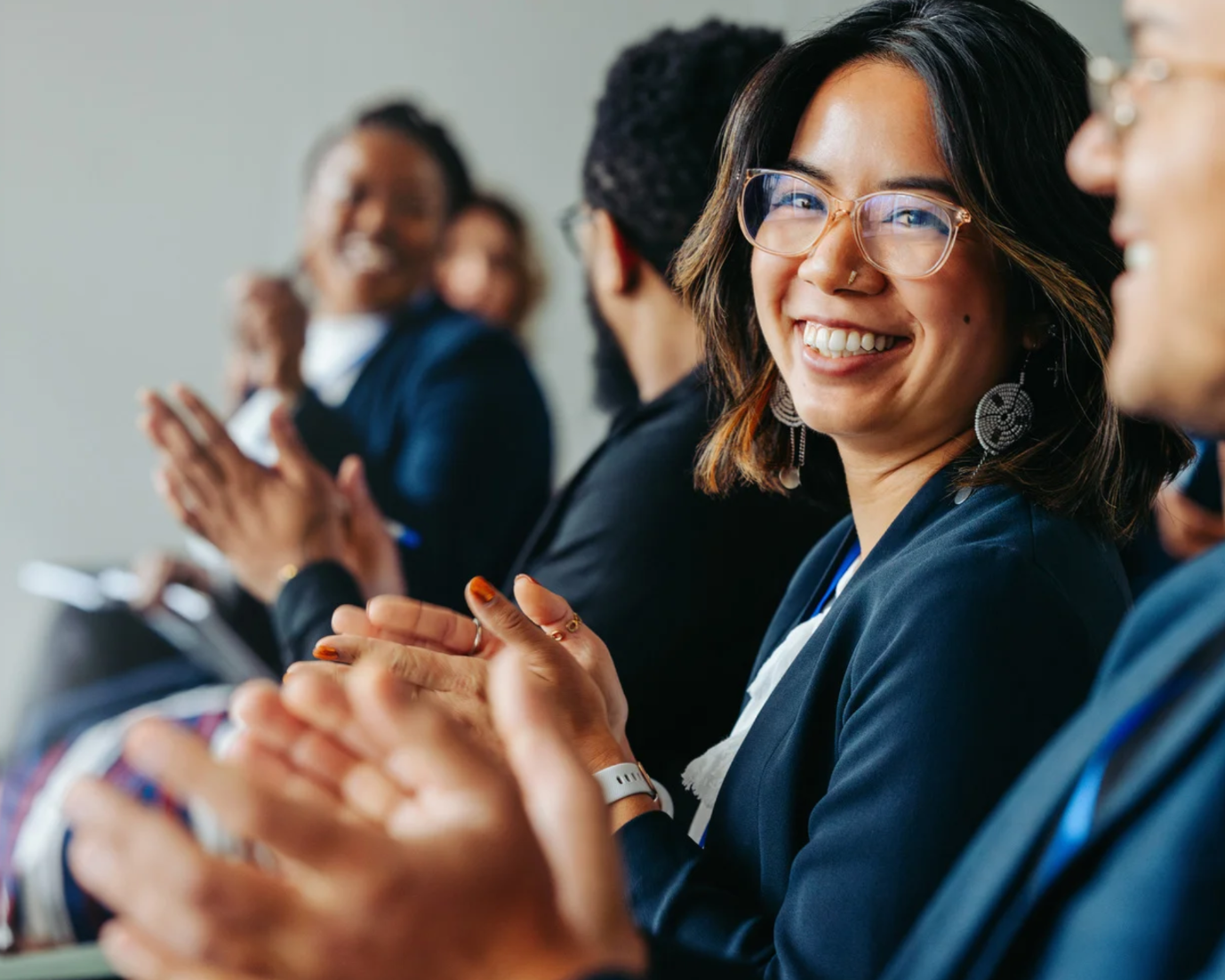 Women wearing glasses, smiling, sat in a crowd clapping