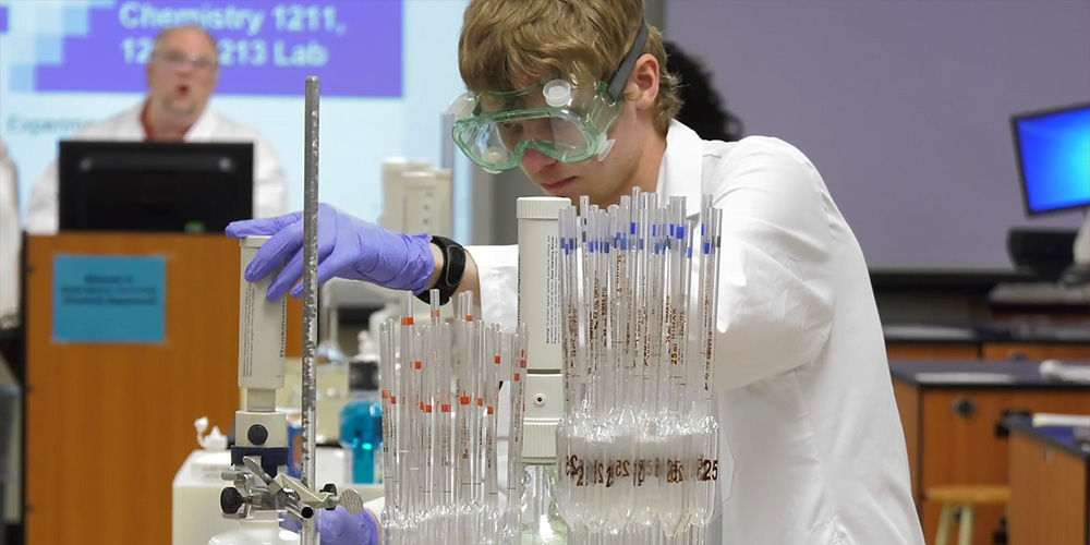 A student wearing safety glasses examines test tubes.